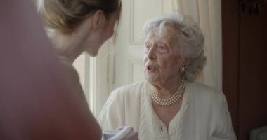 Çok nesilli kadınlar birlikte konuşuyor. Yaşlı büyükanne kadın penceresinin yakınında çay veya kahve içme ziyaret torunu ile gülümseyen. Evde beyaz saçlı yaşlı büyükanne.4k yavaş hareket