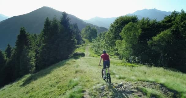 Motoros lovaglás Mountain Bike mentén erdei ösvény légi kilátás nyáron napsütéses napon. Sífutó motoros. Légi MTB kerékpáros lovaglás a nyomvonalat. Lovaglás Mountain e-Bike mentén ösvényen a hegyek — Stock videók