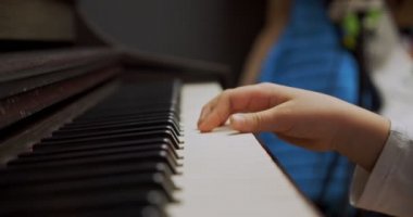 Evde piyano çalan küçük bir kız. Çocuk oturma odasında piyano çalıyor. Çocuk evde piyano öğreniyor. Müzik dersi, yakın çekim, yan görüş..