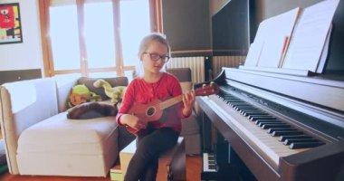 Evde gitar çalan küçük bir kız. Evde müzik aleti ile çocuk portresi. Çocuklar gitar parasını evde ödemeyi öğrenirler..