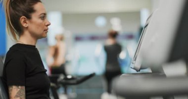 Kadın, spor salonunda eliptik çapraz antrenörle egzersiz yapıyor. Yan görüntü, yavaş çekim. Eliptik bisiklette kadın eğitimi. Spor salonunda pedal çeviren kadın.