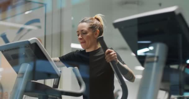 Mujer haciendo ejercicio con la máquina de caminar elíptica en el gimnasio.Vista frontal, cámara lenta. Mujer entrenando en la máquina de caminar. Mujer caminando en la máquina de gimnasio — Vídeo de stock