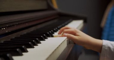 Evde piyano çalan küçük bir kız. Çocuk oturma odasında piyano çalıyor. Çocuk evde piyano öğreniyor. Müzik dersi, yakın çekim, yan görüş..