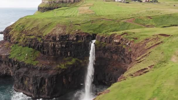 Потрясающий водопад, брызгающийся с высоты обрыва. Водопад Мулафоссур возле деревни Гасадалур на Фарерских островах. Передняя воздушная съемка, дневной свет, облачная погода — стоковое видео