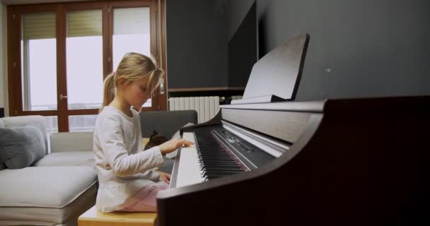 En liten flicka som spelar piano hemma. Han spelar piano i vardagsrummet. Barn lär sig piano hemma. Musiklektion, mediumbild från sidan. — Stockvideo