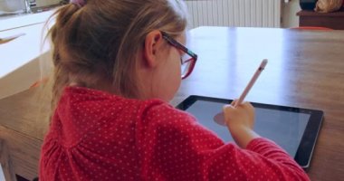 Evdeki tablete resim çizen küçük kız. Uzaktan eğitim için mutfakta tablet cihazına resim çizen çocuk. Tabletle ödev yapan bir kız. Akıllı eğitim. Evde okul var. Uzaklık öğrenimi