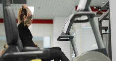 Kadın, spor salonunda eliptik çapraz antrenörle egzersiz yapıyor. Yan görüş, yavaş çekim. Eliptik bisiklette kadın eğitimi. Spor salonunda pedal çeviren kadın.