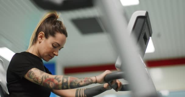 Žena cvičení s eliptický cross trenér na tělocvičně. Boční pohled zblízka, zpomalený pohyb. Trénink žen na eliptickém kole. Žena šlapání v posilovně — Stock video