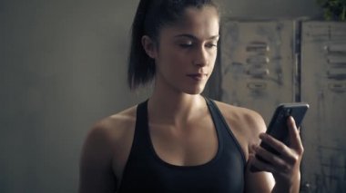 Kadın evde özel antrenör uygulaması olan akıllı telefon kullanıyor. Kadın spor yapmak için fitness uygulamasını kullanıyor. Yörüngeye yakın çekim. Kadın spor yaparken cep telefonu kullanıyor. 