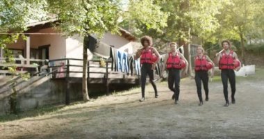 Nehir kıyısında rafting yapmaya başlamak için nehirde yürüyen can yelekleri giyen dört arkadaş. Kameraya doğru yürüyen can yelekleri giyen insanlar. Rafting macera sporu.