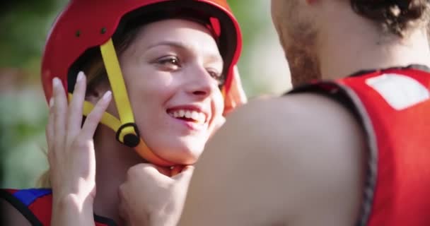 Hombre ayuda a la mujer a usar casco deportivo y chaleco salvavidas antes de descenso de rafting de aguas bravas. Gente con chalecos salvavidas. Rafting deporte extremo. De cerca. — Vídeos de Stock