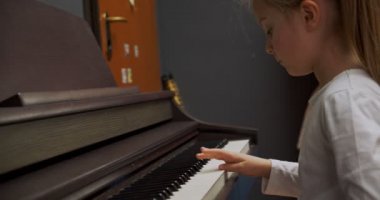 Evde piyano çalan küçük bir kız. Çocuk oturma odasında piyano çalıyor. Çocuk evde piyano öğreniyor. Müzik dersi, yan görünümü kapatın..