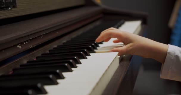Menina tocando piano em casa. O miúdo toca piano na sala de estar. Criança aprendendo piano em casa. Aula de música, close up of hand, vista lateral . — Vídeo de Stock