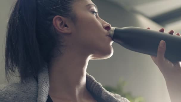 Mulher fitness beber de garrafa esporte durante uma pausa treino em casa ou ginásio. Fechar retrato retroiluminado de mulher ativa bebendo de garrafa de água enquanto descansa do treinamento — Vídeo de Stock