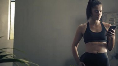 Kadın evde özel antrenör uygulaması olan akıllı telefon kullanıyor. Kadın spor yapmak için fitness uygulamasını kullanıyor. Yörüngeye yakın çekim. Kadın spor yaparken cep telefonu kullanıyor. 