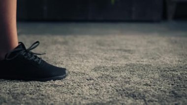 Kadın halıda yürüyor ve kameranın önünde duruyor. Kadın ayaklarının spor ayakkabıları giyip kameranın önünde durmasının ayrıntıları. Ev içinde. Kapatın..