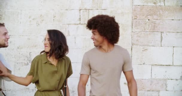 Cuatro turistas felices caminando, sonriendo y divirtiéndose cerca de una pared de ladrillo en la ciudad rural de Spello.Grupo de personas caminando. viaje italiano en Umbria.4k cámara lenta — Vídeo de stock