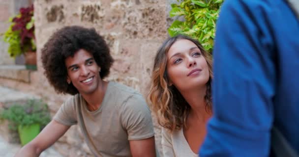 アフリカ系アメリカ人の男性が外で笑っています。スペロルの田舎町のレンガの壁の近くで、 3人の観光客が話して、笑って、楽しんでいます。イタリアの友人旅行。 4kスローモーション — ストック動画