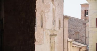 İtalya 'nın tarihi Spello kasabasındaki ortaçağ binaları ve duvar manzarası. Eski İtalyan kasabasında kilisenin olduğu dar bir cadde manzarası. El kamerasıyla.