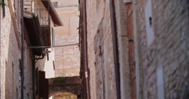 İtalya 'nın tarihi Spello kasabasındaki ortaçağ binaları ve duvar manzarası. Eski İtalyan kasabasında arka planda çan kulesi olan dar bir sokak manzarası. El bilgisayarı sıcak eğiyor.
