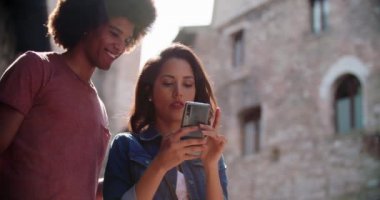 Turistler kırsal kesimdeki konforları ya da simgeleri aramak için akıllı telefon kullanıyor. Yavaş çekim. Kırsal kesimde akıllı telefon kullanırken gülümseyen iki kişi. Orta boy portre fotoğrafı. İtalya 'da arkadaş gezisi.