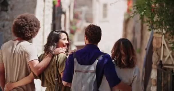 Four happy tourist walking through small street visiting rural town.Back handheld going out of focus while step away.Group of multi ethnic people walking in old town.Vacation in Italy.Sunny weather — Stock Video