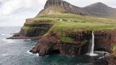 Uçurum manzarasından çarpıcı bir şelale fışkırıyor. Faroe Adaları 'ndaki Gasadalur Köyü yakınlarında Mulafossur şelalesi. İleriye dönük çekim, gün ışığı, bulutlu hava