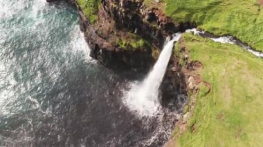 Uçurum manzarasından çarpıcı bir şelale fışkırıyor. Faroe Adaları 'ndaki Gasadalur Köyü yakınlarında Mulafossur şelalesi. Havadan çekim, gün ışığı, bulutlu hava