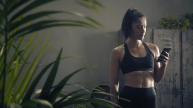 Kadın evde özel antrenör uygulaması olan akıllı telefon kullanıyor. Kadın spor yapmak için fitness uygulamasını kullanıyor. Yörüngeye yakın çekim. Kadın spor yaparken cep telefonu kullanıyor. 