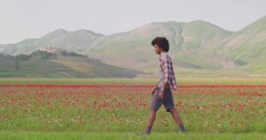 Kırmızı bir çiçek tarlasının yanında yürüyen iki kişi. Kadın dışarıda yürürken omuzlarına atlıyor. Yan görüş. Mutlu kadın, erkeğin üzerine atlıyor şakalaşıyor ve doğa yürüyüşünden zevk alıyor. 