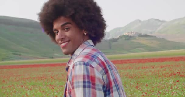 Twee mensen lopen in de buurt van een rood bloemenveld. Glimlachende vrouw springt op vrolijke manschouders terwijl ze buiten loopt.side view detail. HAppy vrouw springen op man grappen en genieten outdoor wandelen — Stockvideo