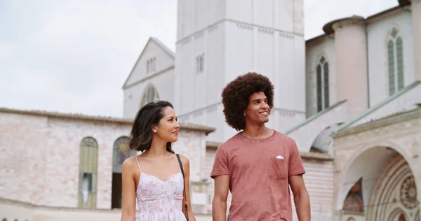 Due persone che camminano insieme sorridendo nella giornata di sole. Uomo e donna che camminano e sorridono. Coppia romantica che cammina con campanile sullo sfondo. Handheld Slow motion close shot.Viaggio con gli amici in Italia. Foto Stock