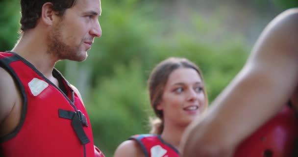 구명 자켓을 입은 행복 한 그룹의 사람들이 이야기하고, 강을 건너기 전에 미소짓는다. 사람들의 그룹은 극단적 인 스포츠 활동을 시작하기 전에 브리핑 한다.. — 비디오