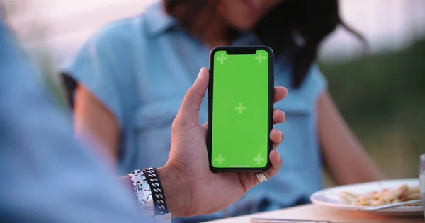 Uomo che utilizza il dispositivo smartphone schermo verde durante una romantica cena all'aperto al tramonto. Foto Stock