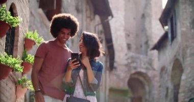 Turistler kırsal kesimdeki konforları ya da simgeleri aramak için akıllı telefon kullanıyor. Yavaş çekim. Kırsal kesimde akıllı telefon kullanırken gülümseyen iki kişi. Orta boy portre fotoğrafı. İtalya 'da arkadaş gezisi.