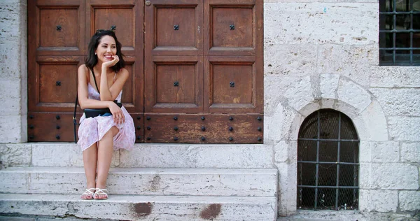 Een vrouw die op de trap van de ingang van de stad zit. Toeristische vrouw rustend bij de ingang van het oude gebouw in landelijke stad.slow motion medium shot.Friends reis in Italië. — Stockfoto