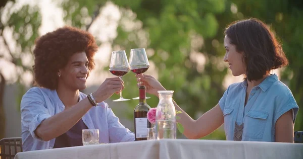 Hombre y mujer tostando y bebiendo vino tinto durante la cena gourmet romántica al aire libre al atardecer. Amigos italiano viaje — Foto de Stock