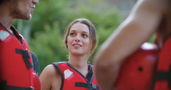 Feliz grupo de personas con chalecos salvavidas hablando, sonriendo antes de rafting descenso del río.Grupo de personas sesión informativa antes de comenzar la actividad deportiva extrema.Rafting deporte extremo.Sun backlight mano. — Foto de Stock