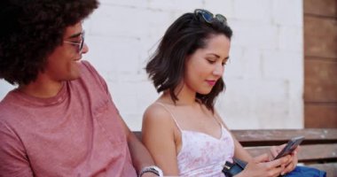 İki gülümseyen insan akıllı telefon kullanarak bankta dinleniyor. Turistler bankta dinleniyor. Kırsal kesimdeki bankta oturan adam ve kadın cep telefonu kullanıyor. Yavaş çekim..