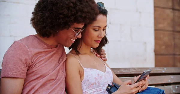 Duas pessoas sorridentes sentadas no banco descansando usando smartphone. Turistas descansando em bench.Man e mulher usando telefone celular sentado na cidade rural bench.slow movimento close shot.Friends viagem na Itália. — Fotografia de Stock