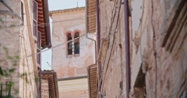 İtalya 'nın tarihi Spello kasabasındaki ortaçağ binaları ve duvar manzarası. Eski İtalyan kasabasında arka planda çan kulesi olan dar bir sokak manzarası. El kamerasıyla.