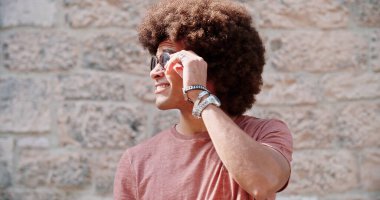 Taş duvarın önünde güneş gözlüğü takan Afro-Amerikan erkek portresi. Güzel, mutlu bir adam portresi taşra kasabasında.. 