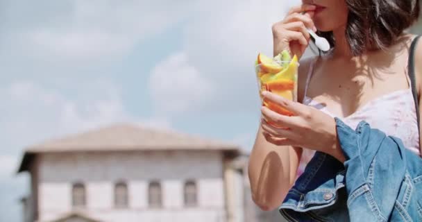 Mujer comiendo ensalada de frutas en la ciudad o en el casco antiguo. Turista tener un descanso comiendo una ensalada de frutas en un día soleado. Detalle de la mujer recogiendo con tenedor una ensalada de frutas — Vídeos de Stock