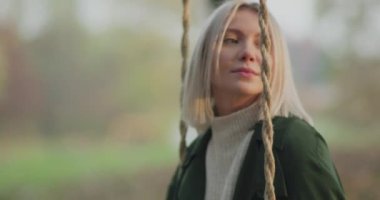 Kadın salıncakta sallanıyor, gülümsüyor gün batımına bakıyor. Yavaş çekim