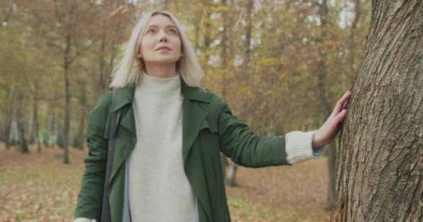 Jeune femme blonde timide marche sur les feuilles pour corde swing en automne. Belle fille se balançant dans le parc. Mouvement lent, vue latérale — Video