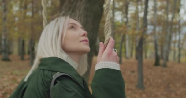 Ein junges Mädchen schwingt im Herbst inmitten eines Parks. Schöne Mädchen lächeln.Zeitlupe, Seitenansicht. — Stockvideo