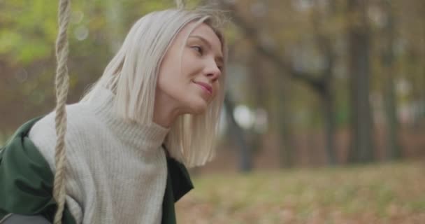 Junge Frau schwingt im Herbst in einem Park. Schöne Mädchen lächelt beim Blick auf Horizont.Zeitlupe — Stockvideo