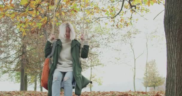 Beautiful woman swinging under a big tree in a cold autumn journey. Back to childhood. slow motion — Stock Video