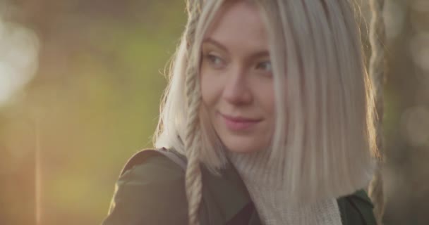 Young woman reads a book on a swing. Blonde and beautiful woman smile at sunset in an autumn day.Memories resurface for a young woman. — Stock Video