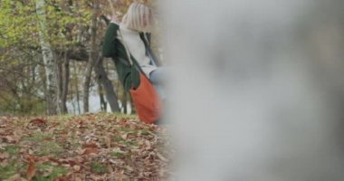 Soğuk bir sonbahar yolculuğunda büyük bir ağacın altında sallanan genç bir kadının yan görüntüsü. yavaş çekim